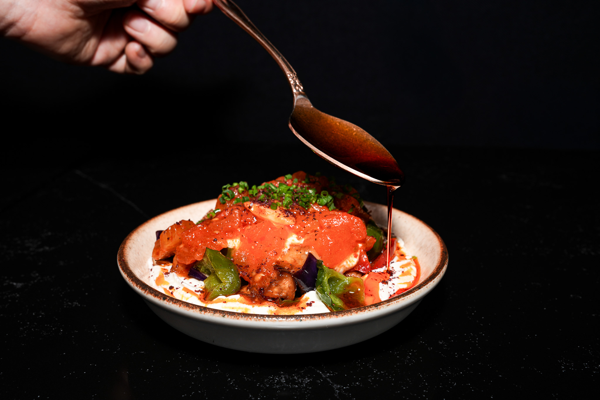 Tomato sauce being spooned over aubergine and yogurt