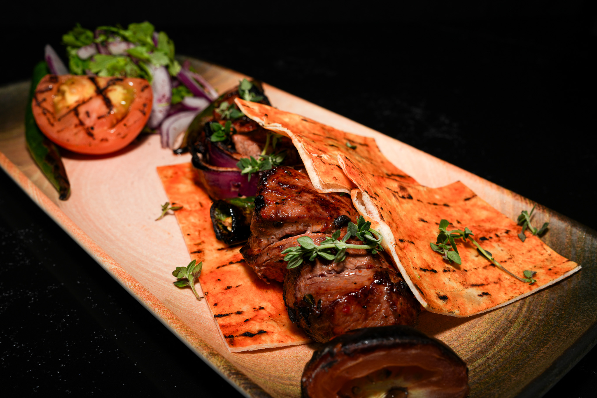 Grilled meat beneath flatbread with tomato and onion salad