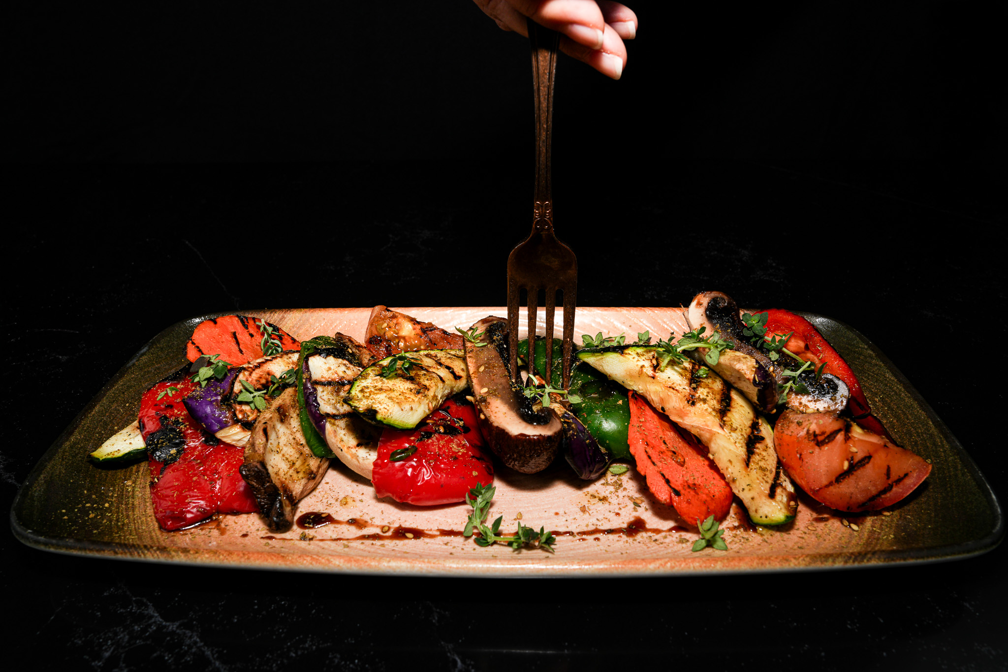 A fork lifting vegetables from a grilled vegetable platter