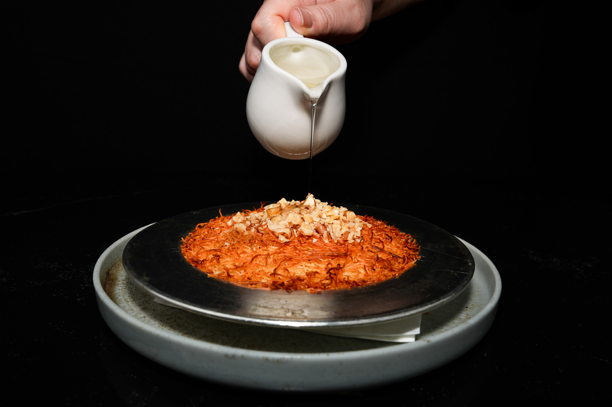 Cream being poured over a golden kunefe