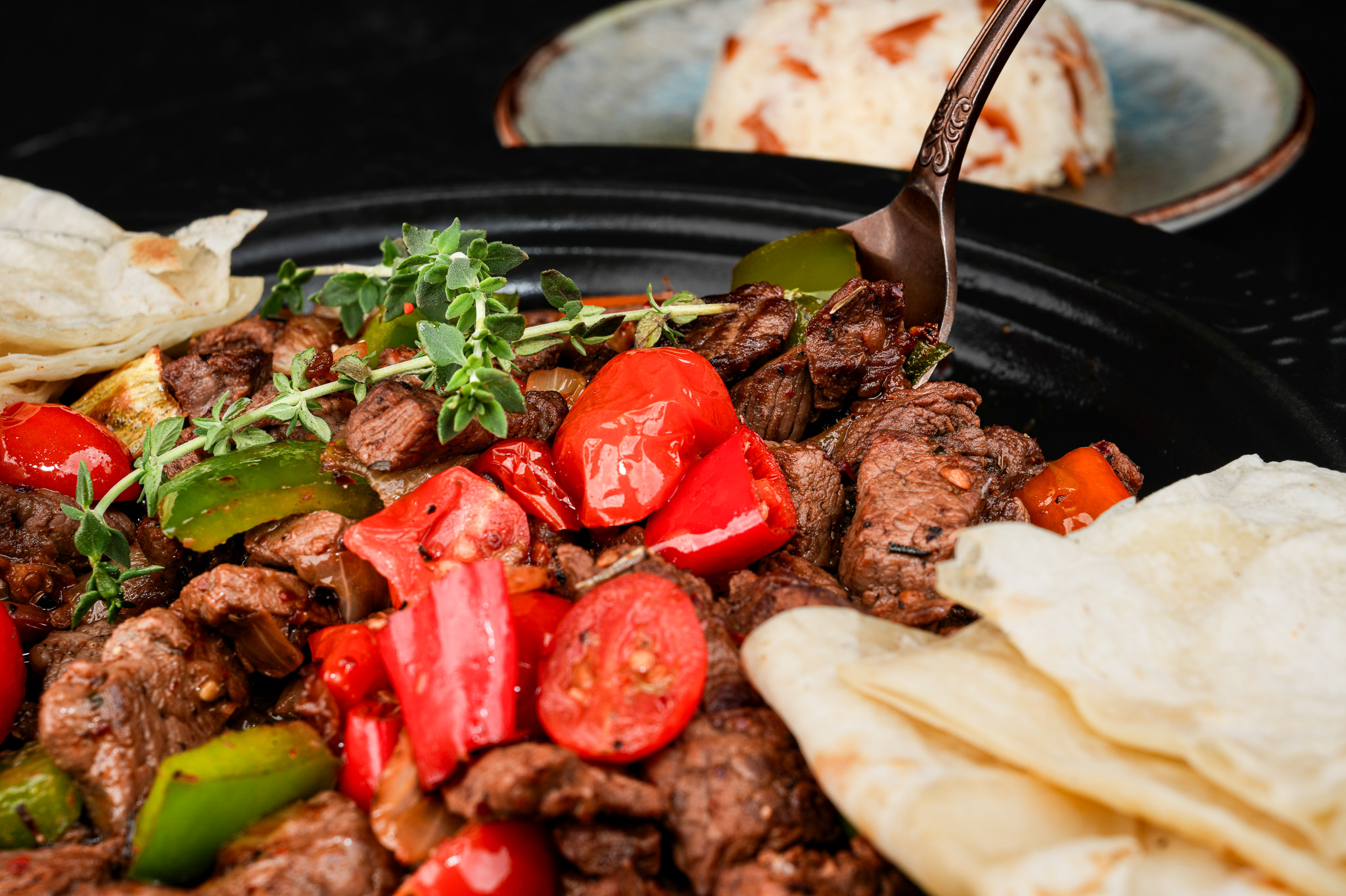 A fork lifting meat from a skillet of tomatoes and peppers
