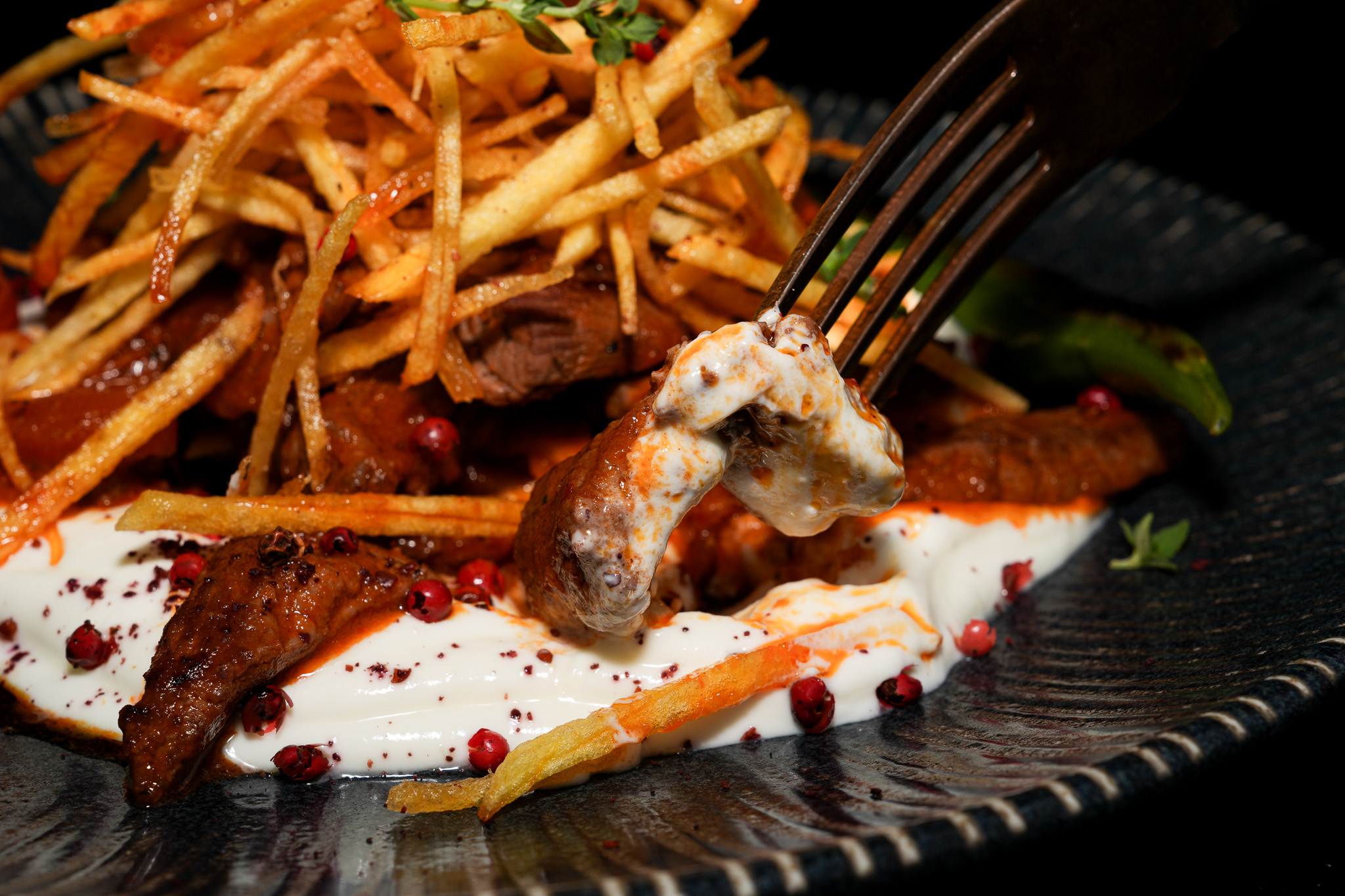A fork lifting meat through yogurt beside crisp potato straws