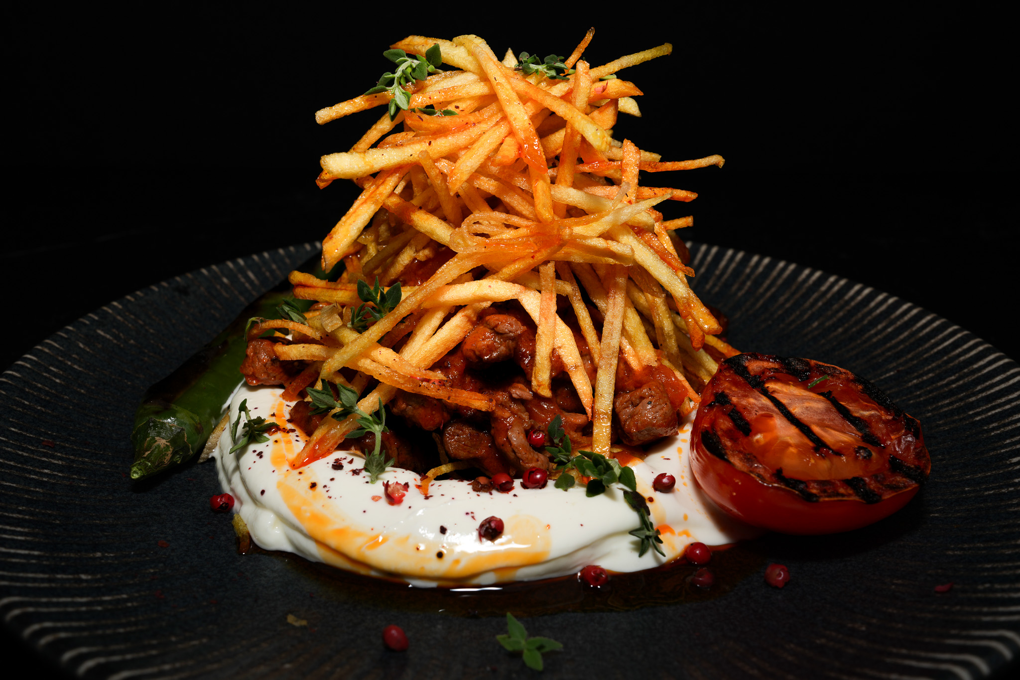 Meat over yogurt topped with crisp potato straws