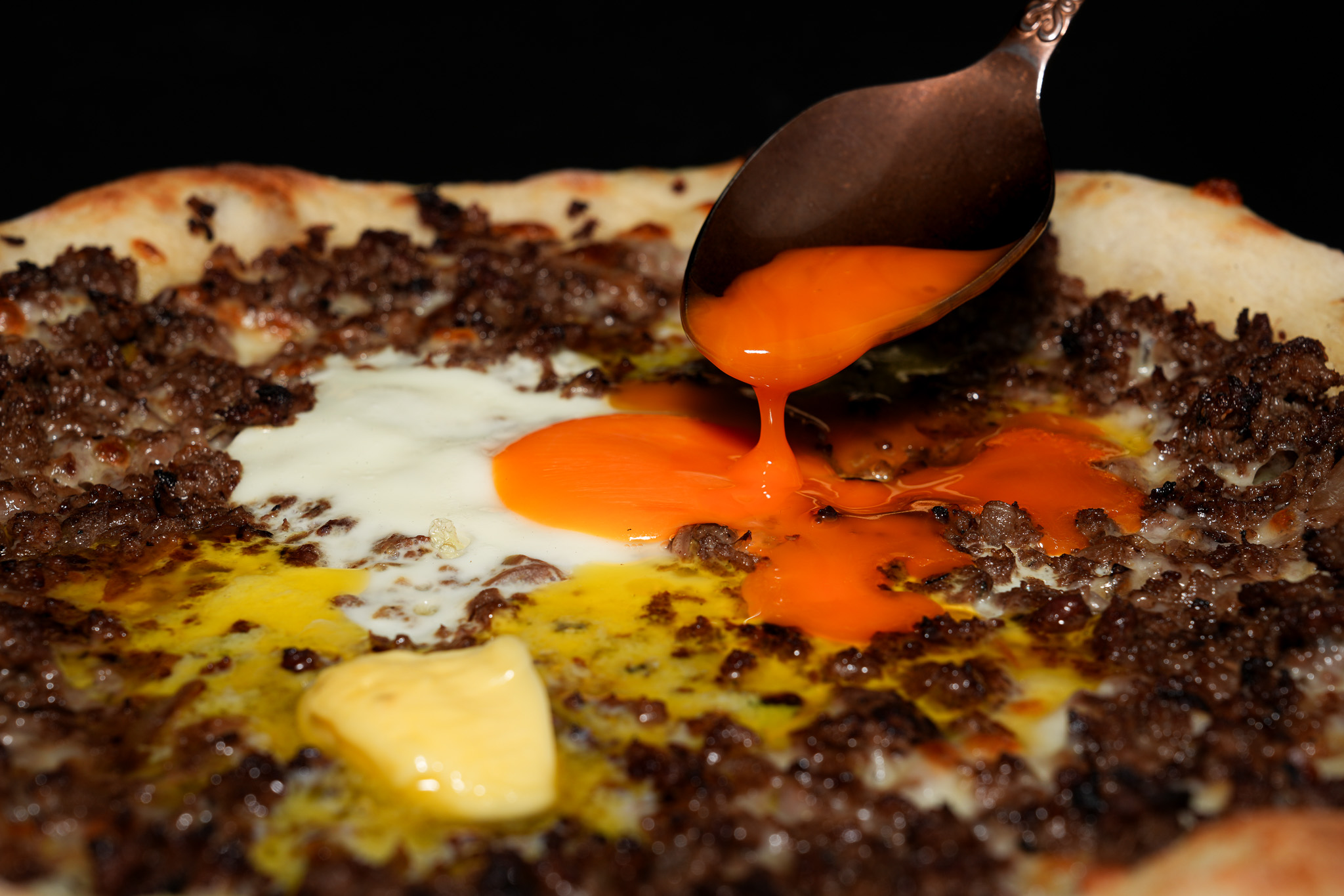 Close-up of egg yolk spreading over minced meat flatbread