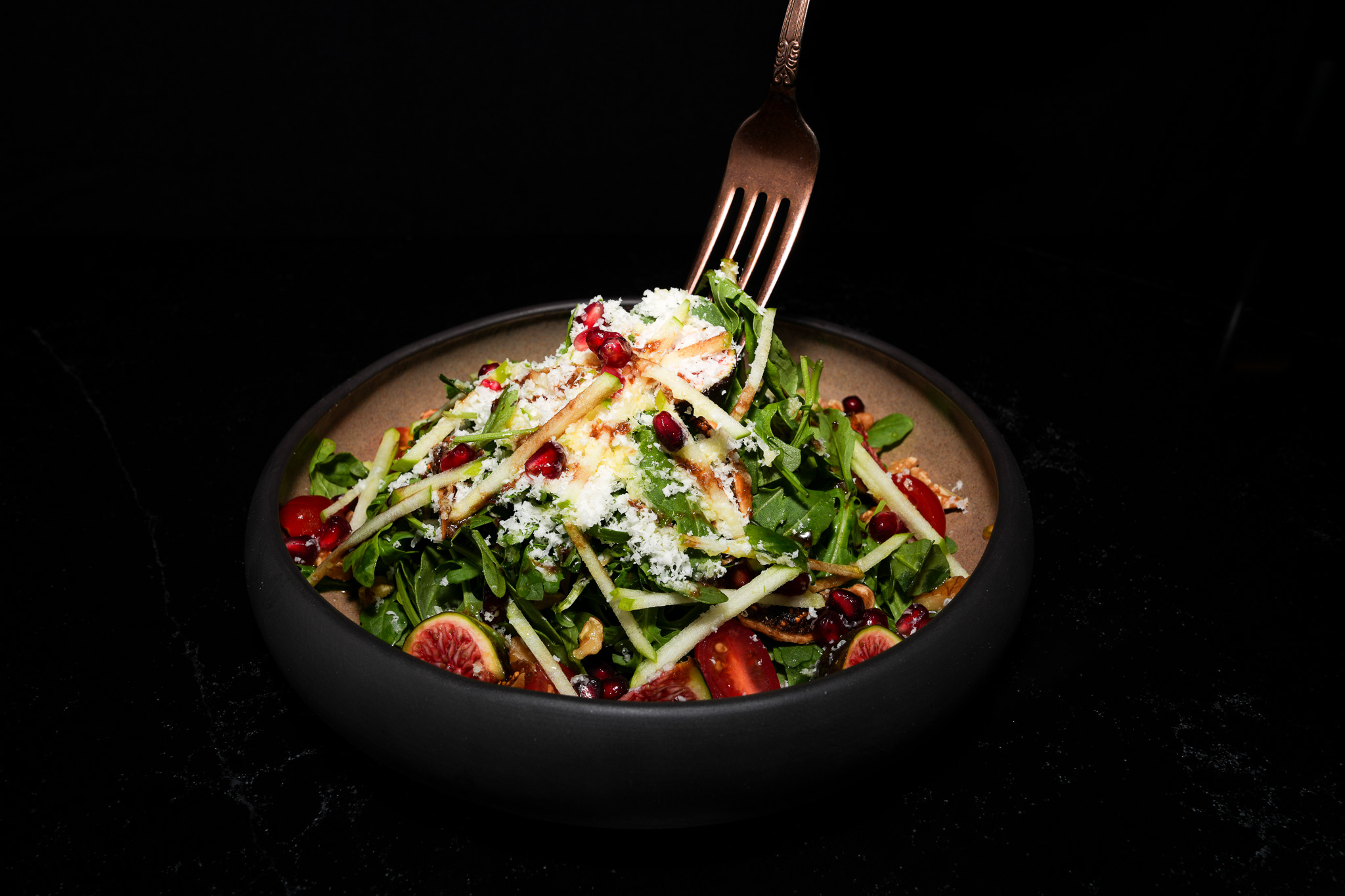 A fork lifting mixed salad with greens, cucumber, and figs