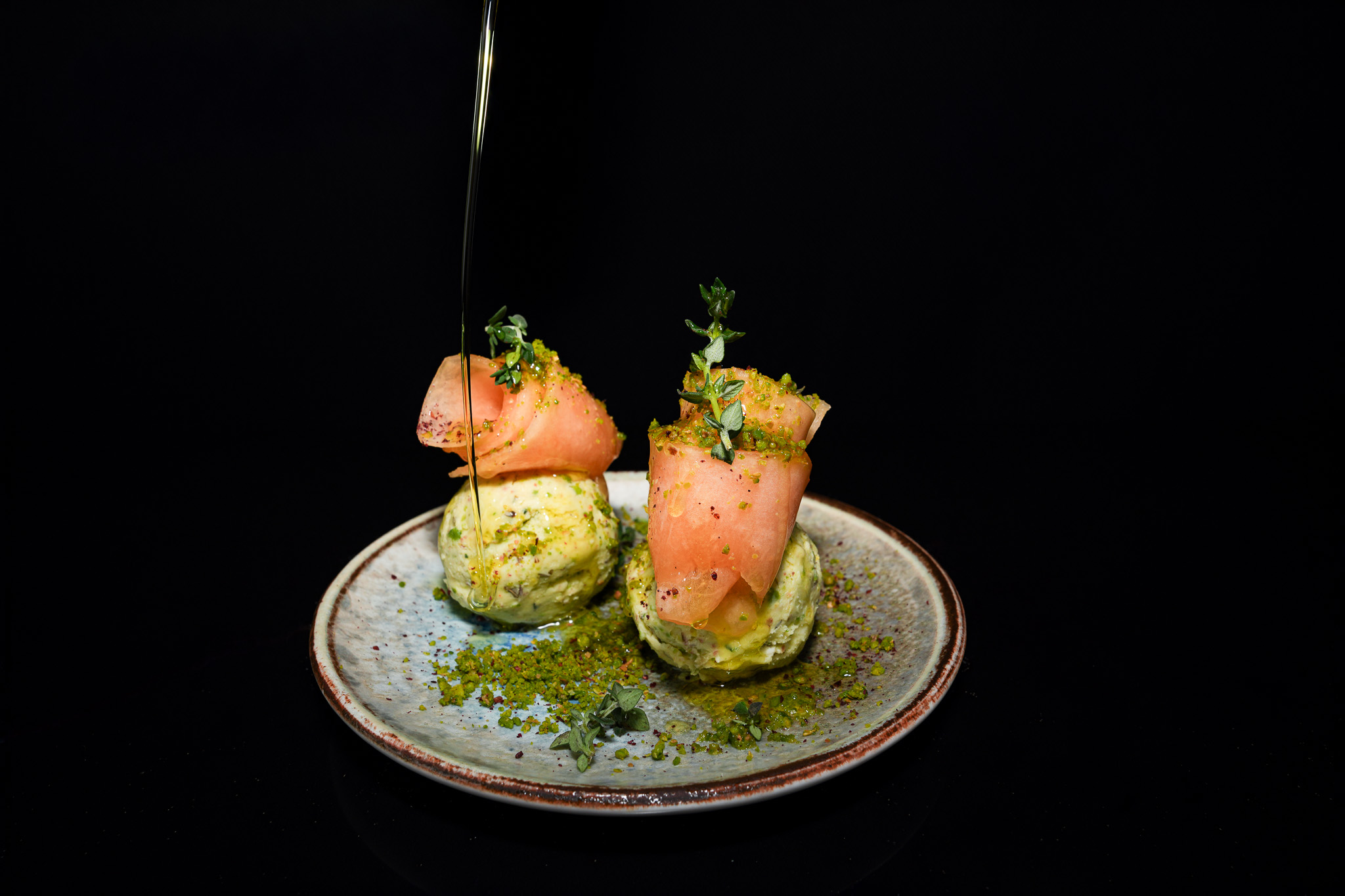 Two salmon-wrapped avocado rolls being finished with oil