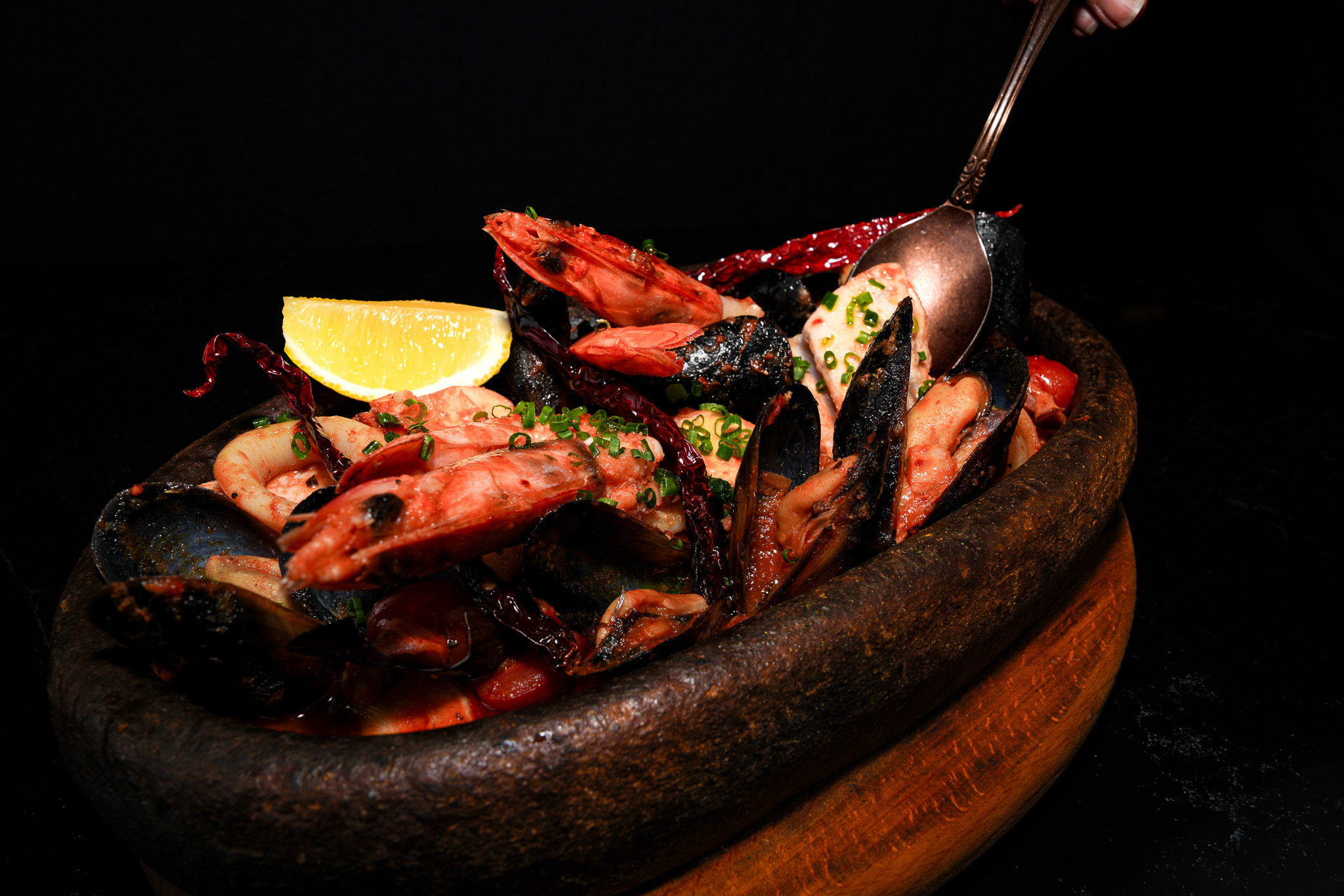 A spoon lifting seafood from a hot skillet with lemon
