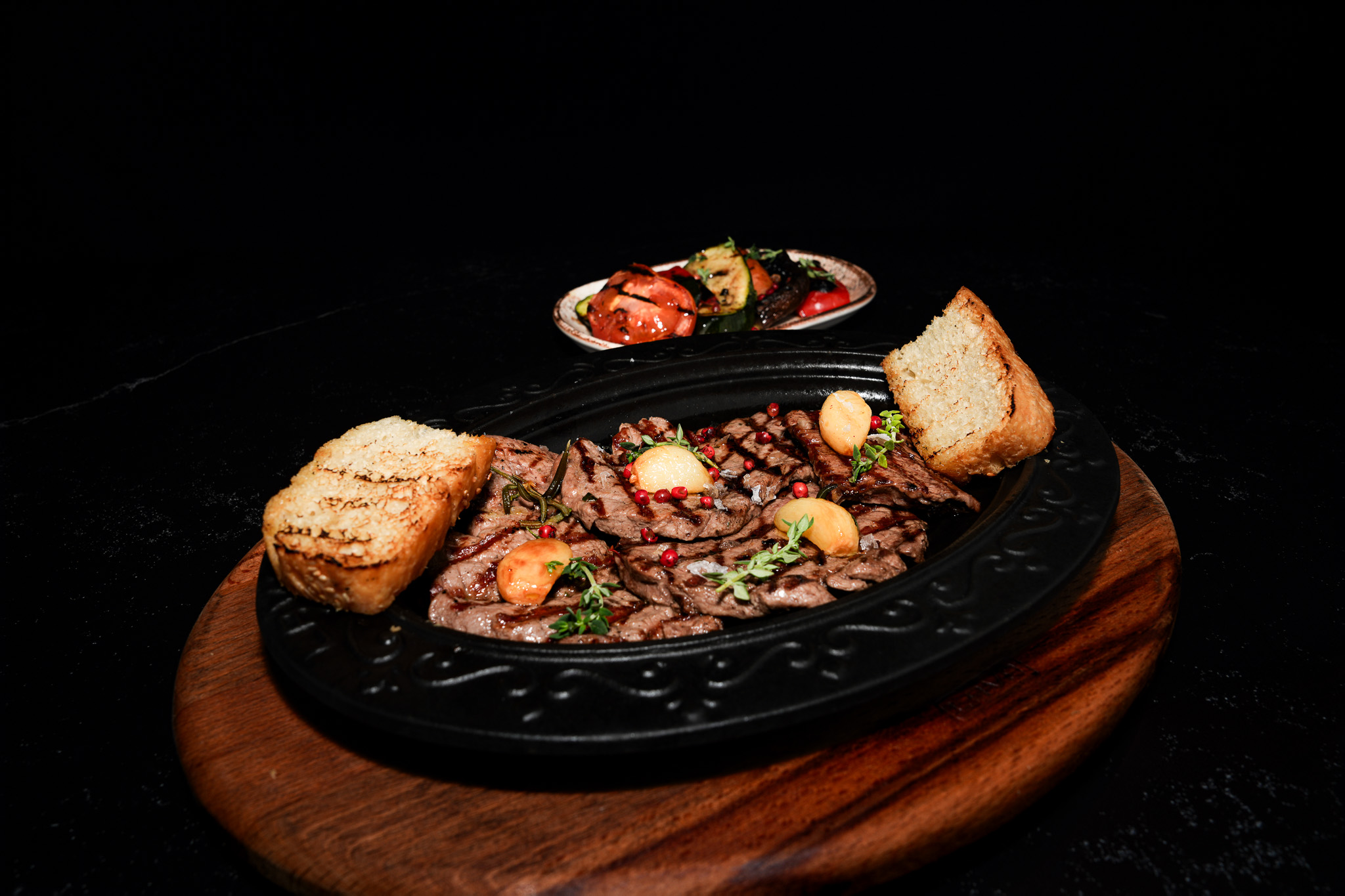 Grilled steak with garlic and bread on a sizzling platter