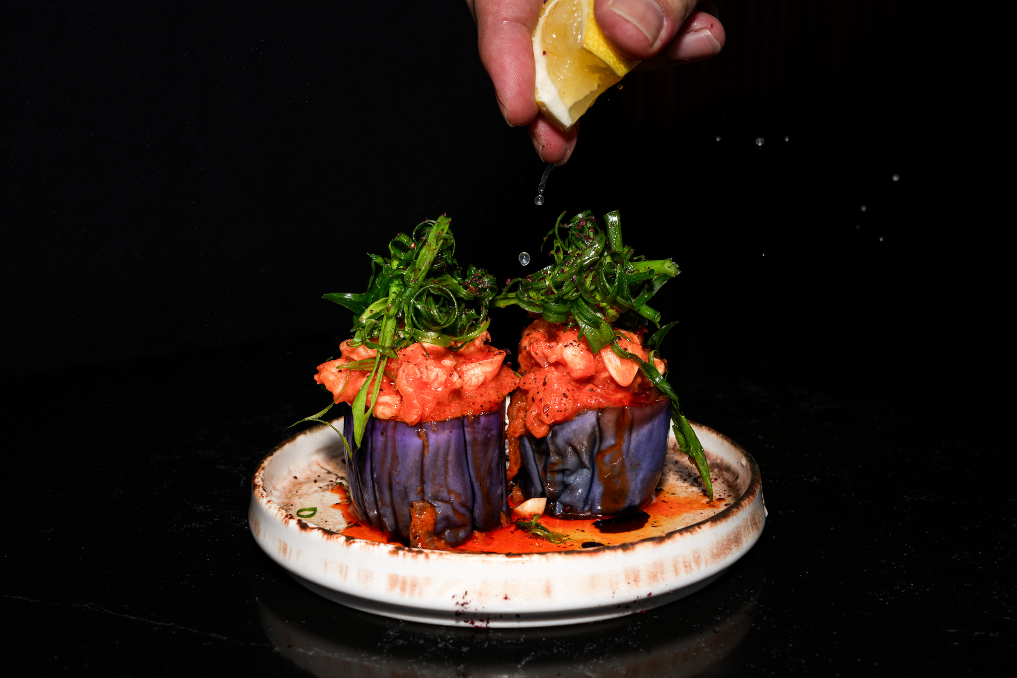 Lemon being squeezed over a stuffed aubergine
