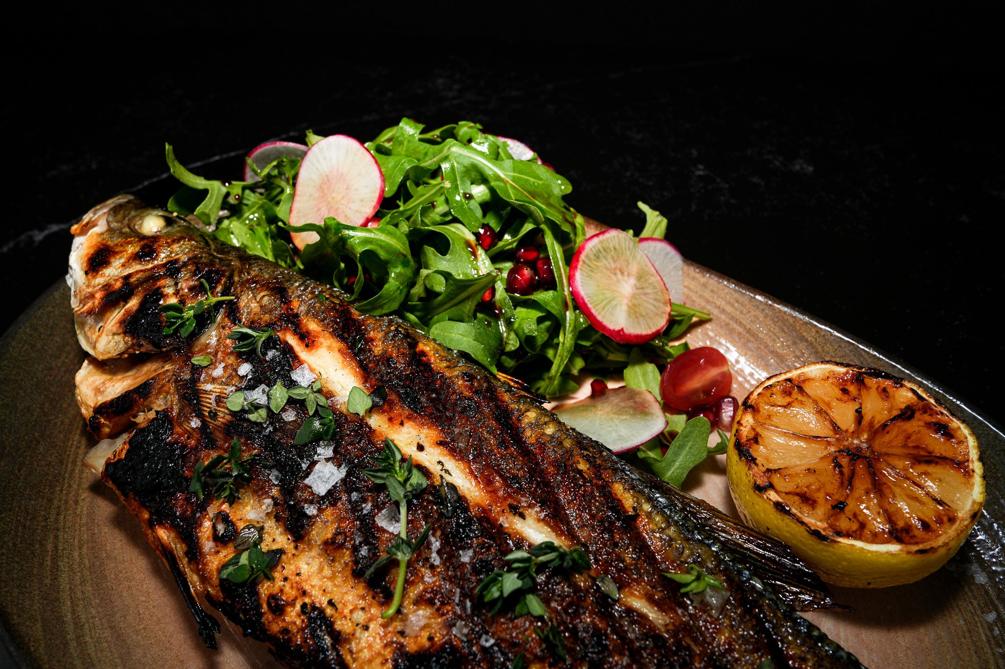 Close-up of whole grilled fish with herbs and lemon