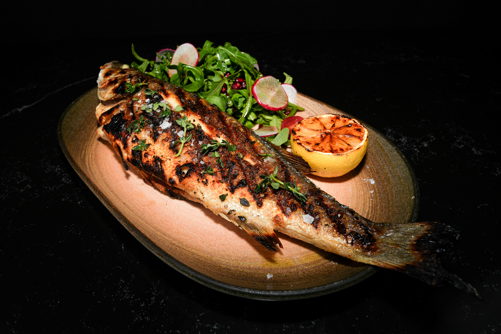 Whole grilled fish served with leafy salad and charred lemon